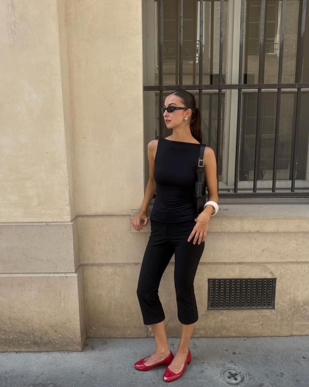 90s retro casual style showing a woman in a fitted black boatneck tank top, black cropped capri pants, and vibrant red ballet flats walking down a city street